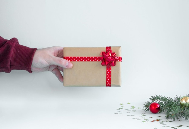 A man's hand holds a gift with a red bow and a satin ribbon in his hand