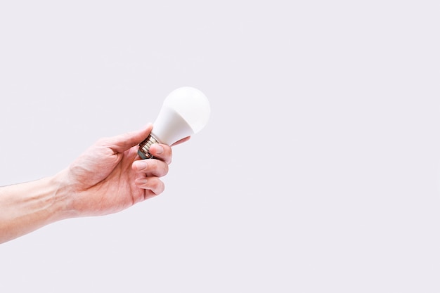 A man's hand holds a light bulb in his hands on gray