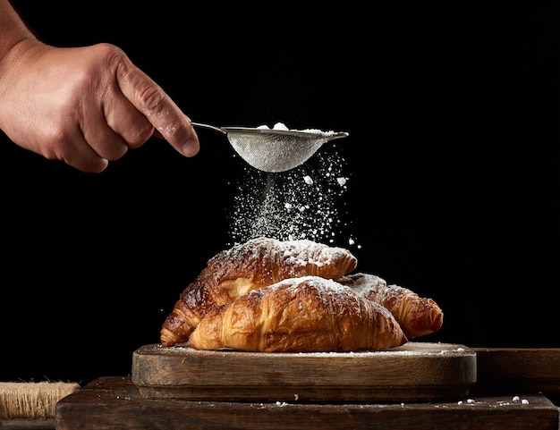 Man's hand holds a metal strainer with powdered sugar