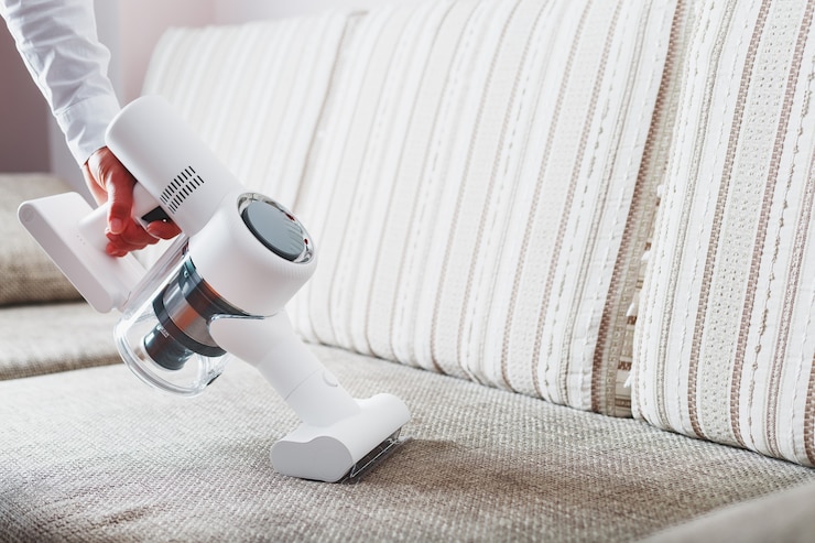Photo a man's hand holds a modern wireless vacuum cleaner for cleaning the sofa in the house.