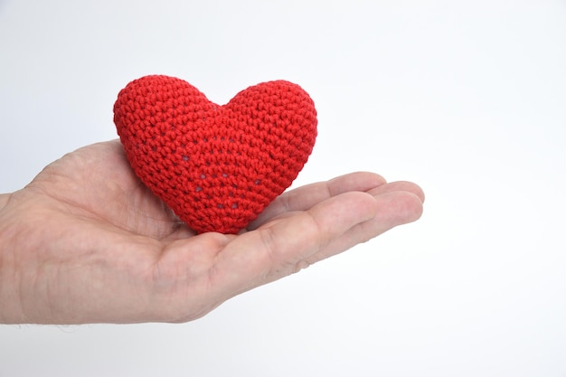 Photo a man's hand holds out a heart knitted of red yarn on the palm image is made on a white background