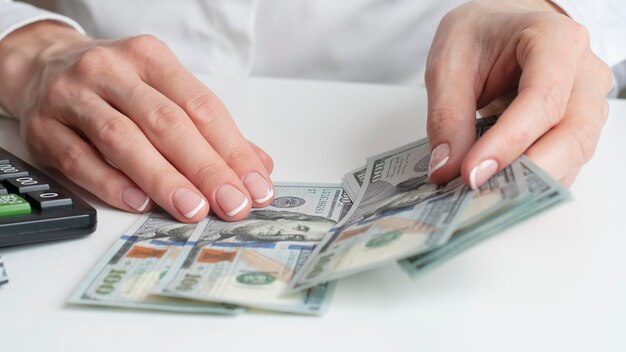 A man's hand holds out one hundred dollar bills against the background of an office table with a computer