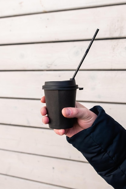 A man's hand holds a paper glass with a hot drink of mulled wine against