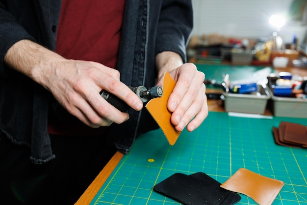 A man's hand holds pieces of leather for a leather wallet in his workshop The process of working with natural brown leather The craftsman holds the craft