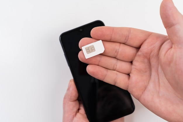 A man's hand holds a SIM card near a black smartphone