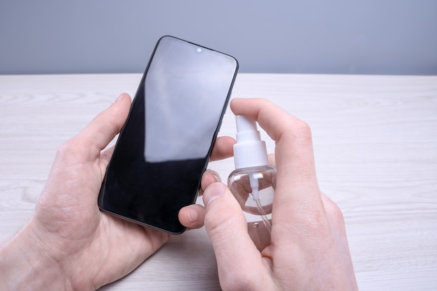 A man's hand holds and snaps a disinfectant spray and disinfect the phone to disinfect various surfaces that people touch.antibacterial antiseptic gel for hands