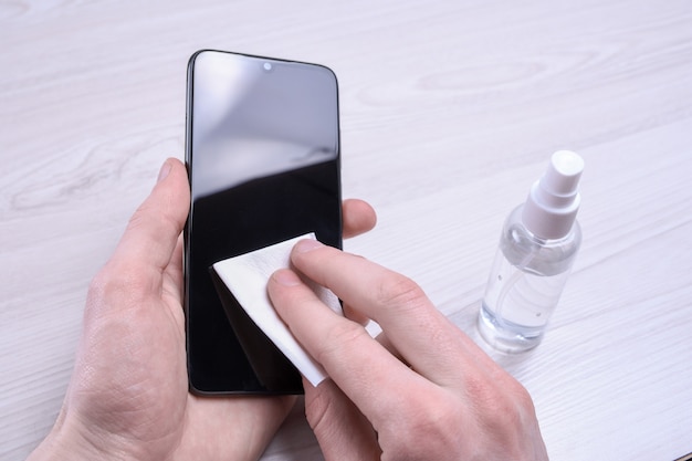 Foto la mano di un uomo tiene e scatta uno spray disinfettante e disinfetta il telefono per disinfettare varie superfici che le persone toccano. gel antibatterico antisettico per le mani