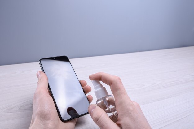 A man's hand holds and snaps a disinfectant spray and disinfect the phone to disinfect various surfaces that people touch