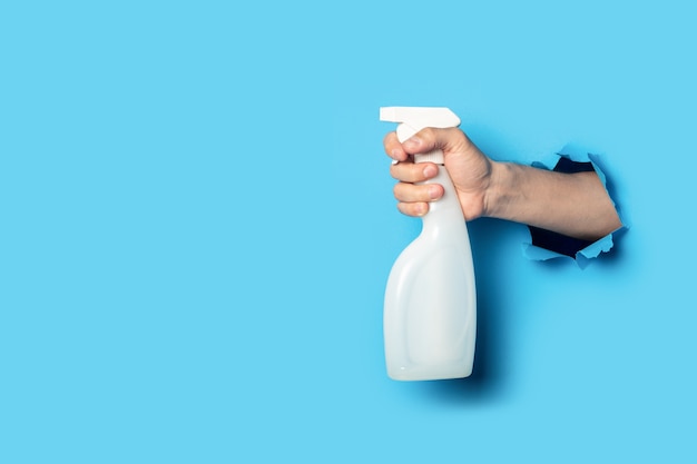 Man's hand holds a spray on a bright blue