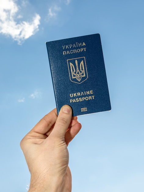 A man's hand holds a Ukrainian passport against the sky