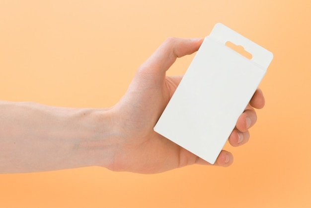 Man's hand holds a white package with a hanging hole on a yellow background Closed Rectangular Gift Yellow Place Isolated Pack Marketing Advertising New Trade Object Rectangle Goods