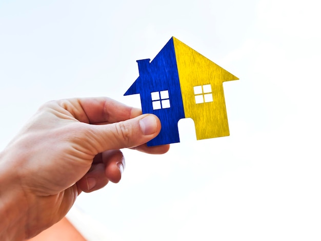 Man's hand holds wooden flat house in Ukrainian flag colors