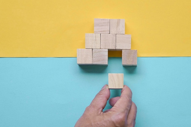 Man\'s hand inserting piece of wood block to complete a pyramid\
shape of wood blocks