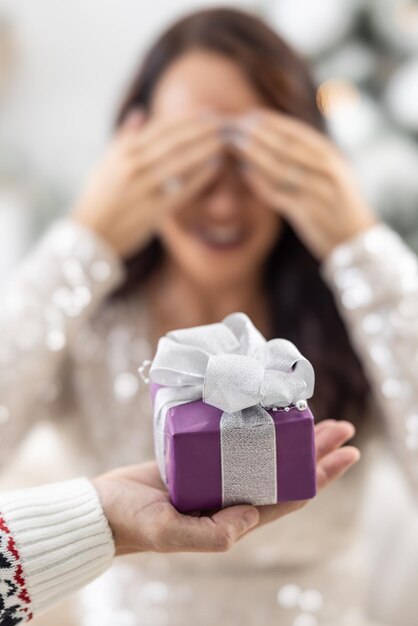 Man's hand is holding purple Xmas present with a ribbon in front of a woman closing her eyes