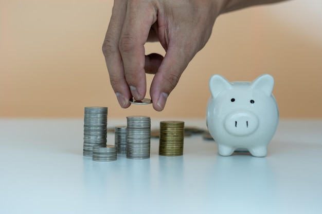 Man's hand is putting coins into a piggy bank to save money saving money for future plans for travel study home and retirement Saving money concept