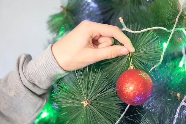 A man's hand in a jumper hangs a red ball on a Christmas tree Holiday at home