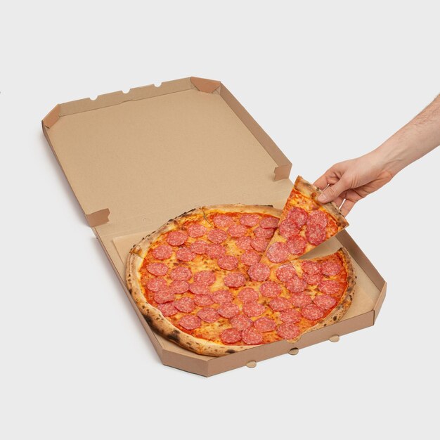 Man's hand met een stuk pepperoni pizza op de achtergrond van een pizzadoos