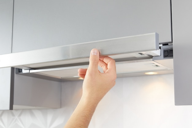 Man's hand opens kitchen hood for cooking or replacing filter. Modern interior on background.