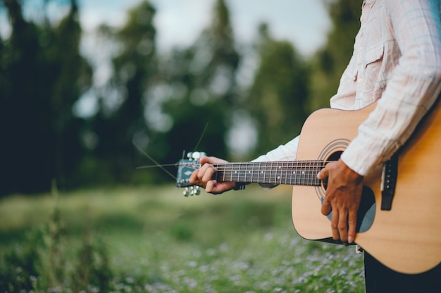 The man's hand plays the acoustic guitar, plays the guitar in the garden alone