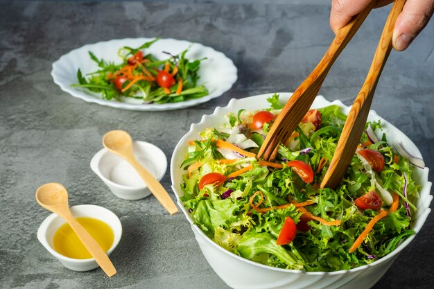 Man's hand serveren salade van sla, tomaten, rugula, diverse groene groenten met houten tang