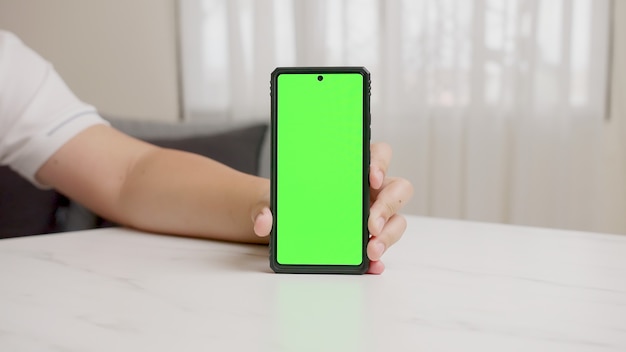 Photo man's hand shows smartphone with green screen in vertical position