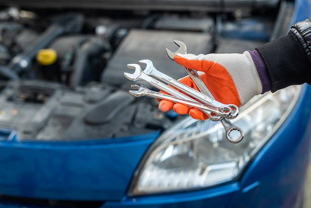 Man's hand in a special glove holds tools for a car near the car Tools concept Car repair concept