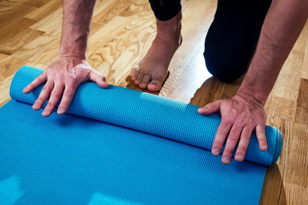 The man's hand spreads the yoga mat on the floor. blue yoga mat