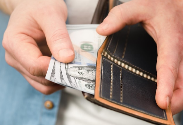 A man's hand takes out one hundred dollar bills from a purse