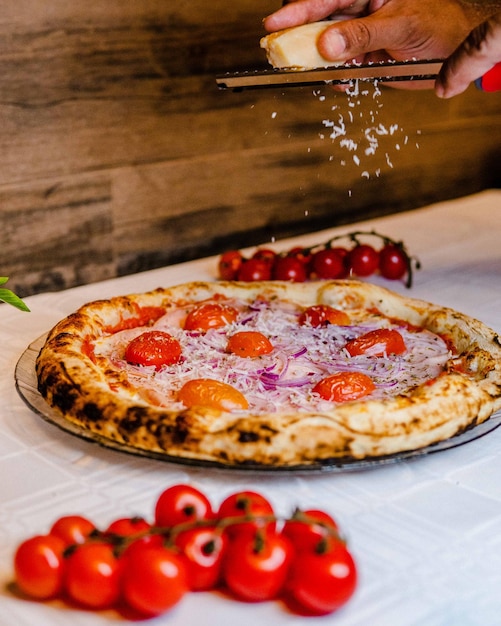 Man's hand topping the delicious pizza with cherry tomatoes with parmesan