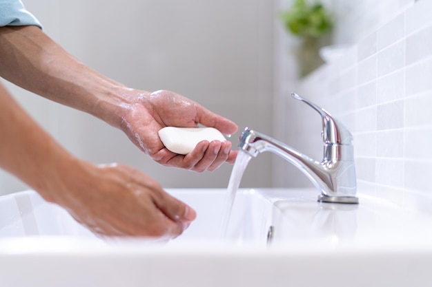 Mano dell'uomo che si lava le mani con sapone e acqua pulita da un rubinetto in bagno lavarsi le mani frequentemente per prevenire la diffusione di germi e per una buona igiene