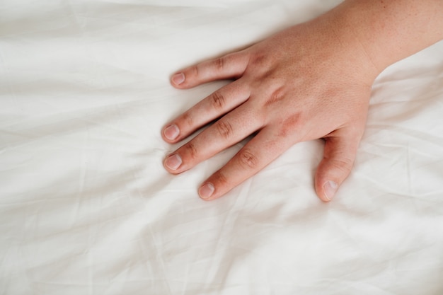 Photo man's hand on a white bed sheet.