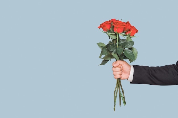 青い背景に赤いバラの花束を持つ男の手