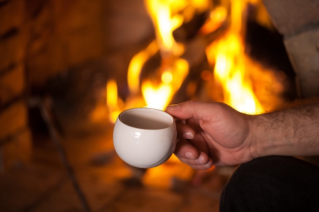 man's hand with a cup by the fireplace.