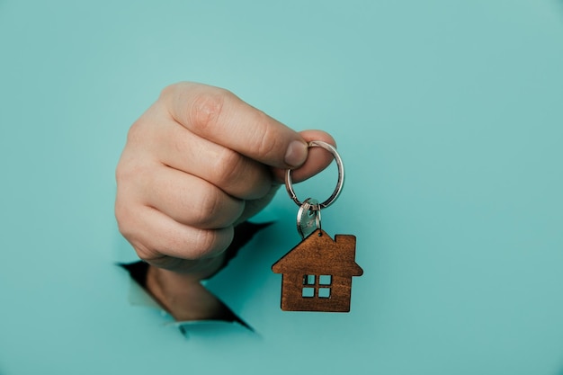 Foto mano d'uomo con la chiave di casa attraverso un buco in sfondo blu vendita di casa e concetto di affitto