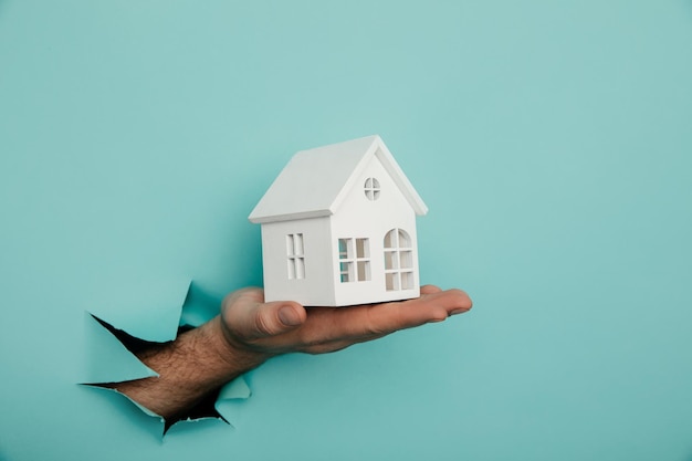 Man's hand with house through a hole in blue paper House sale and rent concept