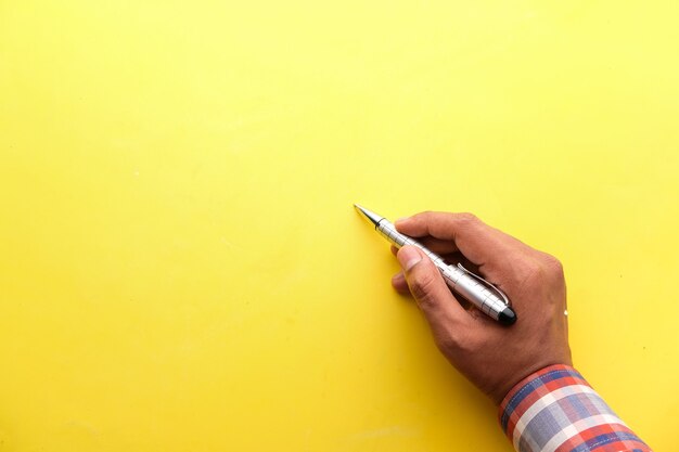 man's hand writing with pen on yellow paper