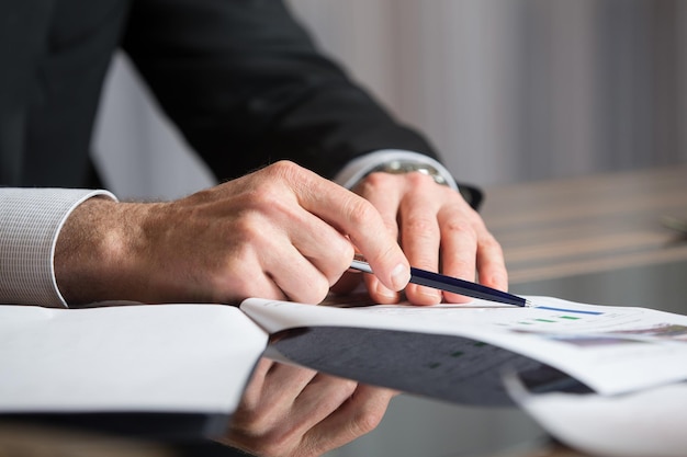 Man's handen met een zwarte pen in beide armen in een denkend gebaar tijdens een vergadering of onderhandeling