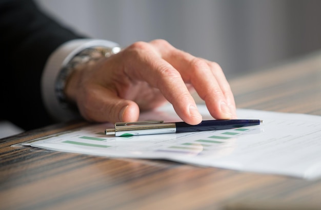 Man's handen met een zwarte pen in beide armen in een denkend gebaar tijdens een vergadering of onderhandeling