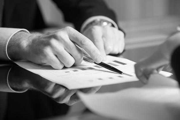 Man's handen met een zwarte pen in beide armen in een denkend gebaar tijdens een vergadering of onderhandeling