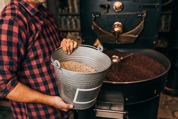 Man's handen met vers gebrande aromatische koffiebonen boven een moderne koffiebranderij.