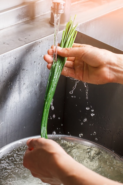 Man's handen wassen groene ui. Groene ui onder waterstroom. Pittig ingrediënt voor salade. Zelfgekweekte kruiden rijk aan vitamines.