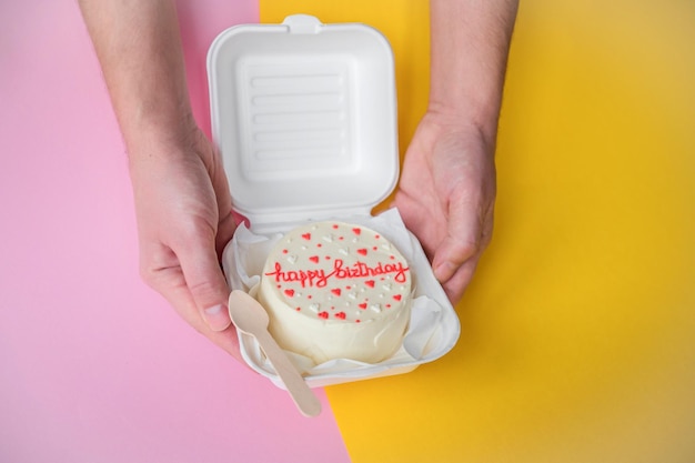 A man's hands hold a festive bento cake with birthday and hearts