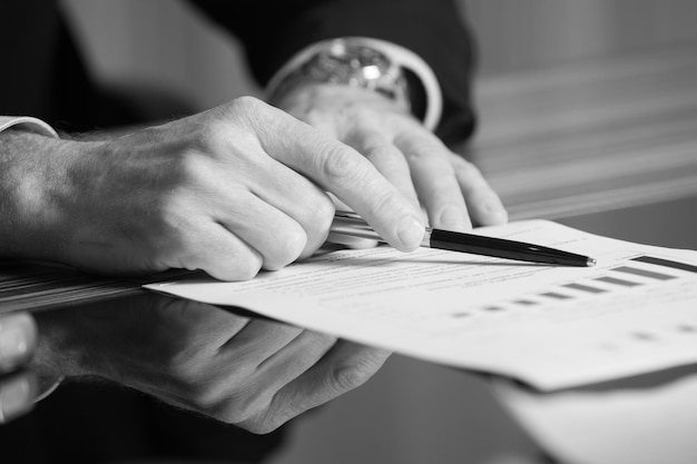 Man's hands holding a black pen in both arms in a thinking gesture during a meeting or negotiation