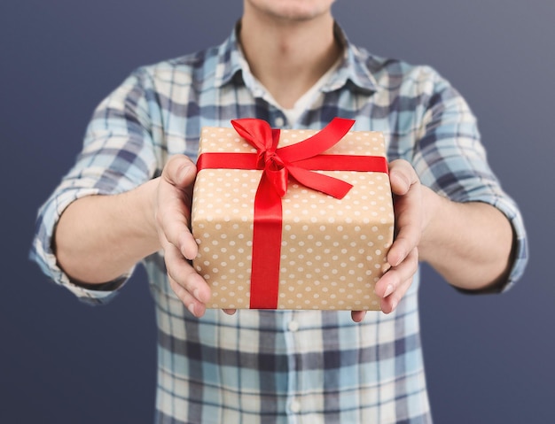 Man's hands holding craft paper gift box with a present for Christmas, new year, valentine day or anniversary on blue background.