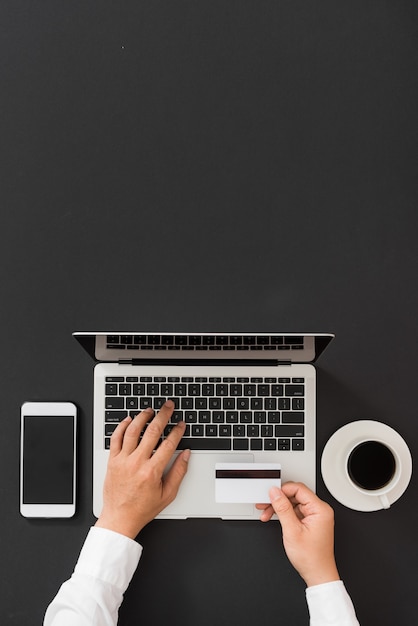 Man's hands holding a credit card. Using laptop for online shopping, flat lay desk concept