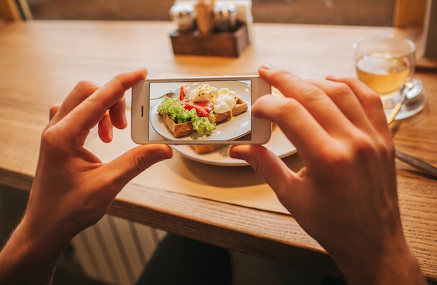 男の手は、携帯電話を保持し、プレートにおいしい食事の写真を撮っています。カラフルで美味しいです。