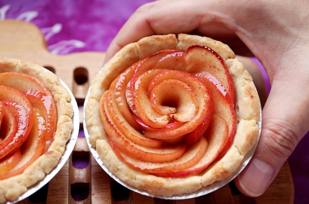 Man's hands placing a fresh baked delectable mini apple rose tartlet on the wooden breadboard