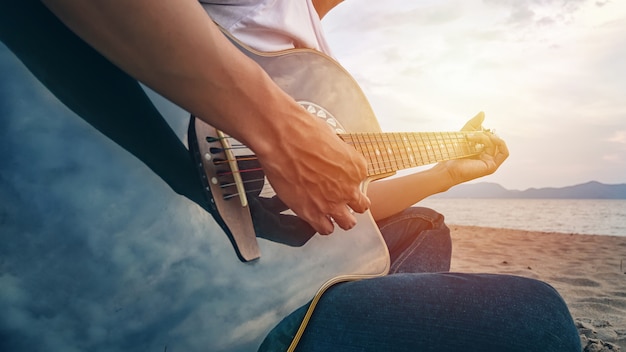 Le mani dell'uomo che giocano la chitarra acustica sulla spiaggia