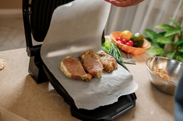 The man's hands prepares delicious juicy meat steak on an electric grill on wooden table Smoke in the home kitchen