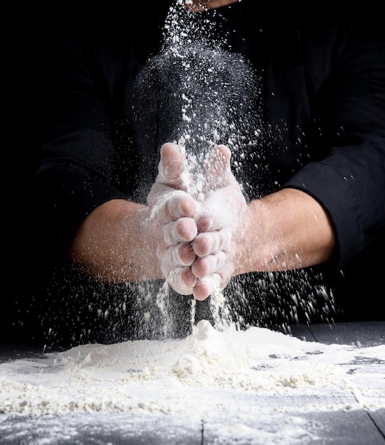 man's hands and splash of white wheat flour on a black background